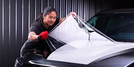 Installateur de covering appliquant un film sur le capot d'un véhicule.

